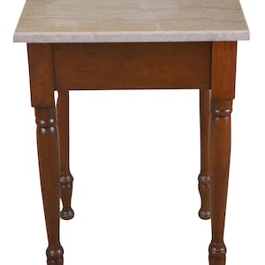 May include: A small, wooden end table with a light brown marble top and turned legs.