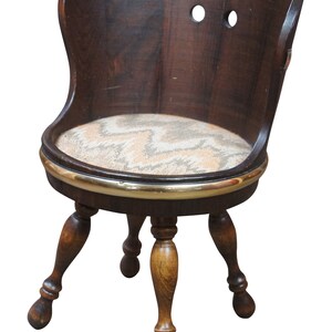 May include: A dark brown wooden chair with a padded seat and a brass trim around the edge. The chair has a curved back and four turned legs.