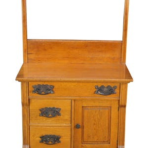May include: A light brown wooden dresser with a mirror frame. The dresser has two drawers, a cabinet door, and ornate metal handles. The mirror frame is supported by two vertical posts and a horizontal bar.