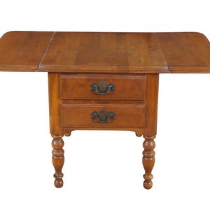 May include: A wooden drop-leaf table with two drawers and turned legs. The table is a warm brown color and features brass hardware on the drawers. The table's top is 36 inches wide when fully extended.