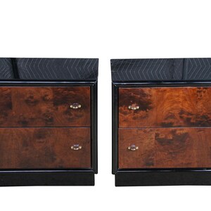 May include: A pair of two-drawer nightstands featuring a high-gloss black frame and top, contrasted with rich brown burl wood drawer fronts. Each drawer is accented with small, clear, oval-shaped hardware pulls centered on the wood panels.