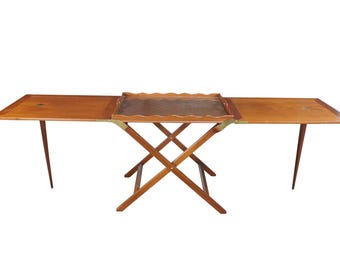 May include: A wooden folding table with a rectangular top and two extendable side leaves. The center features a removable tray with a scalloped edge and a textured surface. The base has a cross-legged design with brass metal hinges.