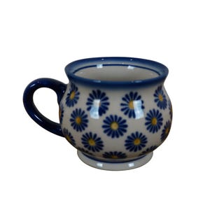 May include: A white ceramic mug with a blue and yellow floral pattern. The mug has a rounded body and a handle.