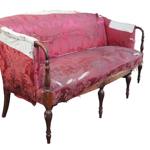 May include: A vintage red velvet sofa with wooden legs and arms. The fabric is worn and faded, showing signs of age and use.