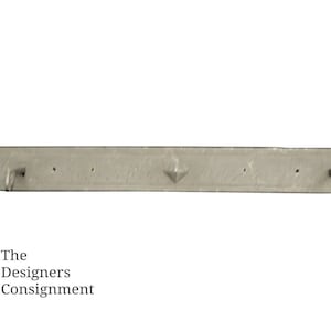 May include: A silver metal wall mounted coat rack with two hooks on each end and three hooks in the middle. The rack has a decorative design with a diamond shape in the center.