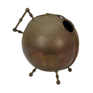 May include: A spherical, antique bronze-colored metal container with a handle and three small legs. The container has a circular opening at the top and is likely a decorative piece or a unique storage vessel.