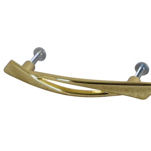 May include: A gold-toned cabinet pull with a curved, abstract design. The pull has a smooth, polished finish and is attached to the cabinet with two screws.