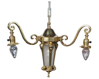 May include: A brass chandelier with two lights and a frosted glass shade. The chandelier has a decorative, ornate design with a scrolled arm and a central, bell-shaped shade.