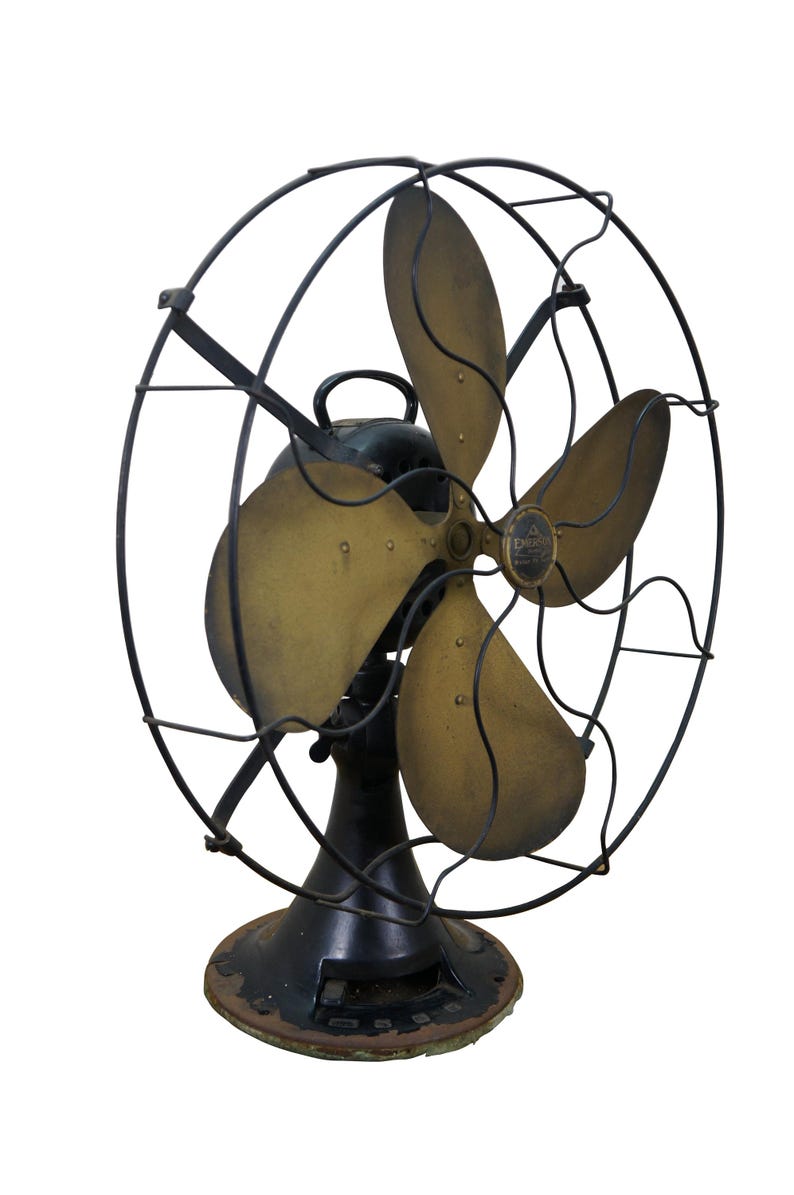Puede incluir: Ventilador el&eacute;ctrico antiguo con cuatro aspas de color lat&oacute;n y una estructura de metal negro. El ventilador tiene una base negra y un asa. Las aspas est&aacute;n ligeramente curvadas, lo que sugiere un dise&ntilde;o vintage.