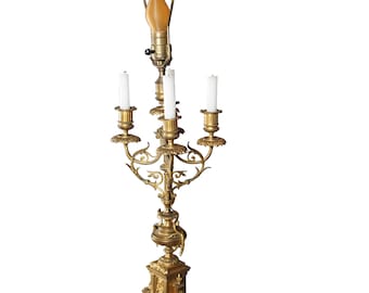 May include: A gold candelabra with four candle holders and a single light bulb on top. The candelabra has a marble base and intricate details.