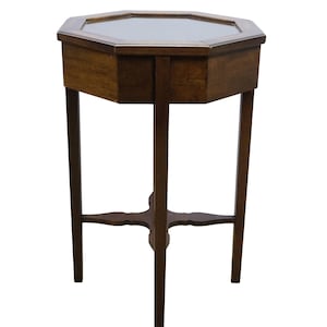 May include: An octagonal side table crafted from dark brown wood, featuring a glass top insert. The table stands on four slender legs connected by a central cross-shaped stretcher, providing a stable base for the flat, multi-sided tabletop surface.