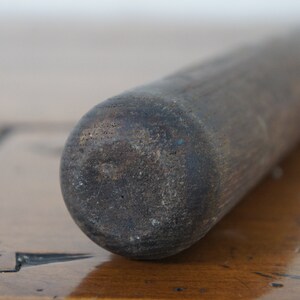 May include: Close-up of a dark brown wooden rolling pin with a rough texture.