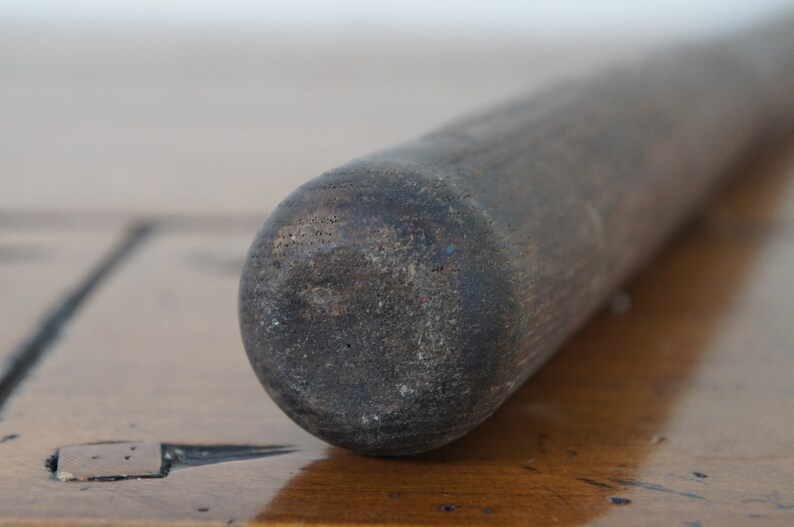 May include: Close-up of a dark brown wooden rolling pin with a rough texture.