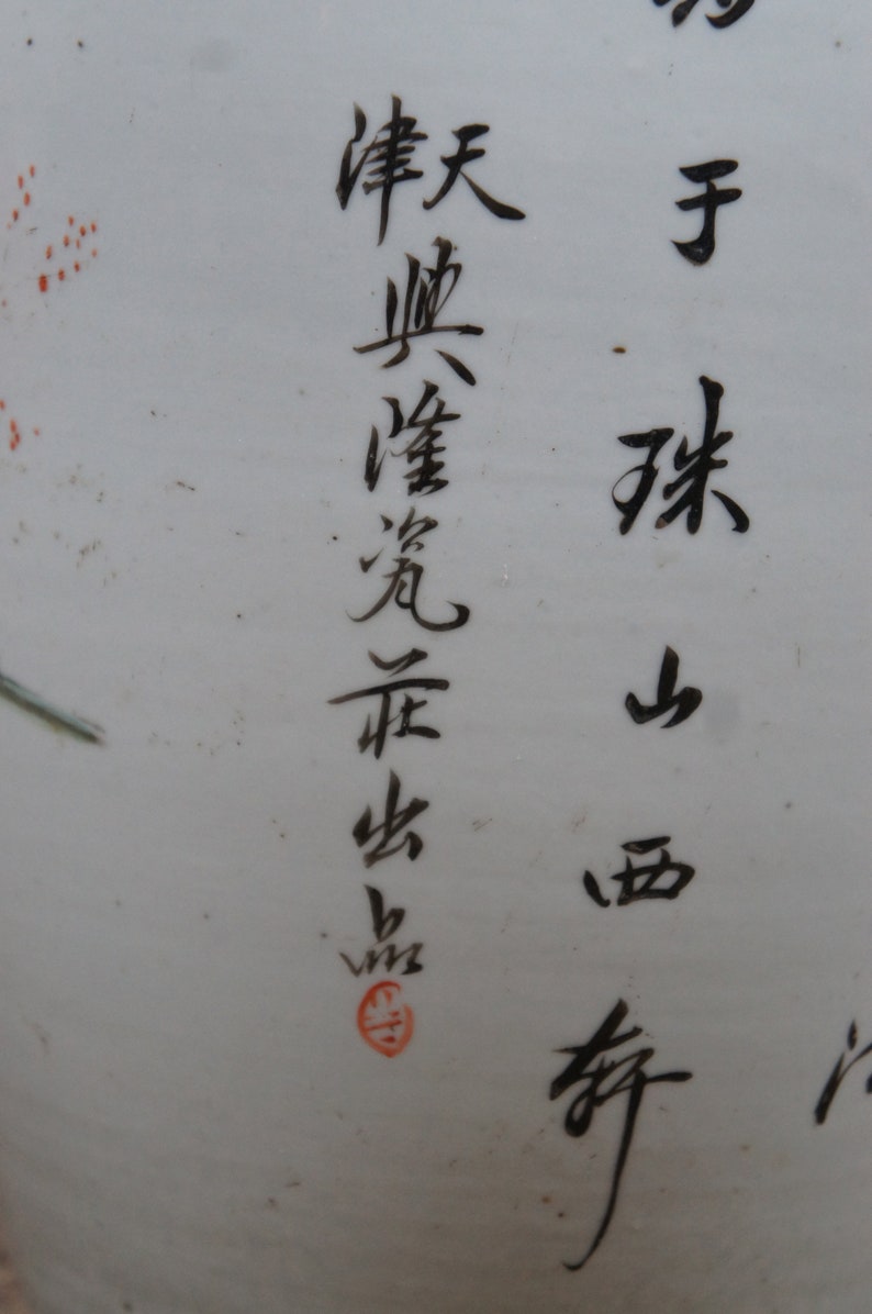 Op de afbeelding: Close-up van een witte keramische vaas met zwarte kalligrafie in Chinese karakters. De karakters lezen "春 天 曉 霞 飛 舟", wat vertaalt naar "Lente ochtend, wolken vliegen, boot". Er is een rode stempel op de vaas.