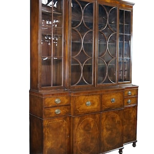 May include: A large brown wooden hutch with glass-fronted upper cabinets featuring circular mullion patterns. The base includes multiple drawers and lower cabinet doors with brass hardware, all finished in a polished wood grain veneer.