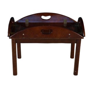 May include: A dark brown wooden butler tray table featuring a rectangular top with hinged, curved side panels that include integrated oval handle cutouts. The table is supported by four straight legs and displays a polished wood grain finish.
