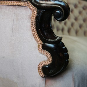 Peut inclure: Gros plan d'un fauteuil vintage avec un accoudoir en bois fonc&eacute; et un rev&ecirc;tement en tissu gris clair. L'accoudoir pr&eacute;sente un motif d&eacute;coratif en forme de volutes et le rev&ecirc;tement a un motif subtil.