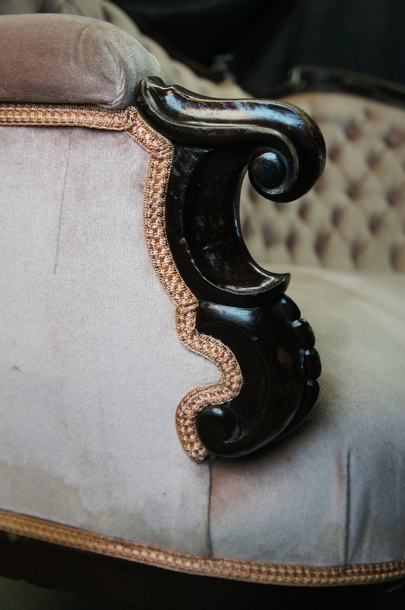 Peut inclure: Gros plan d'un fauteuil vintage avec un accoudoir en bois fonc&eacute; et un rev&ecirc;tement en tissu gris clair. L'accoudoir pr&eacute;sente un motif d&eacute;coratif en forme de volutes et le rev&ecirc;tement a un motif subtil.