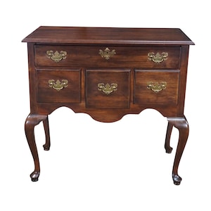 May include: A dark brown wooden chest of drawers featuring a rectangular top, one long upper drawer, and three smaller lower drawers. The piece is accented with ornate brass hardware and supported by four curved cabriole legs.
