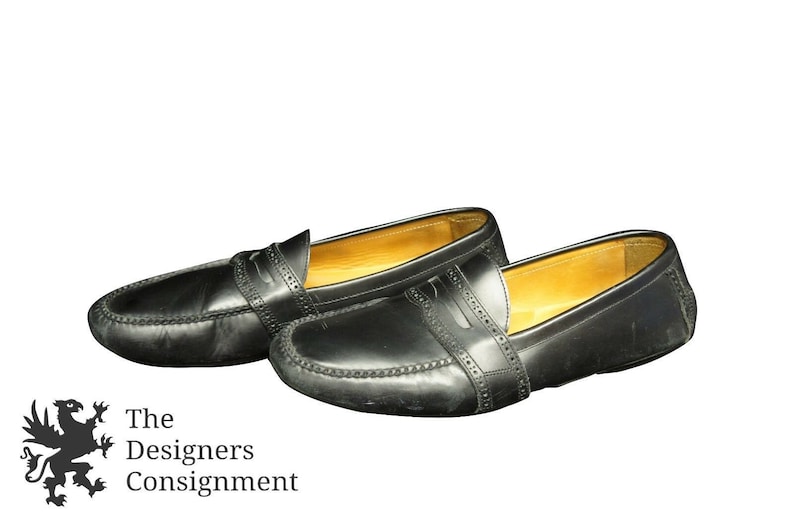 May include: A pair of black leather loafers with a stitched design. The loafers have a brown leather lining and a rounded toe.