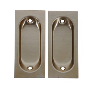 May include: Two brushed nickel flush pull handles with oval openings. The handles are rectangular and have rounded edges.