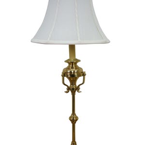 May include: A brass table lamp with a white lampshade. The lamp has a decorative base and stem, and the shade is a classic, slightly tapered shape. The lamp is designed for indoor use.
