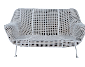 May include: White metal outdoor loveseat with a grid pattern. The seat has a curved back and armrests, supported by thin, rounded legs. The design is reminiscent of mid-century modern furniture.