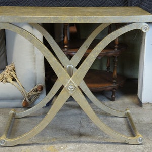 K&ouml;nnte beinhalten: Ein goldfarbener Metalltisch mit rechteckiger Tischplatte und einem X-f&ouml;rmigen Gestell. Der Tisch hat eine Used-Look-Oberfl&auml;che und ist aus Metall.