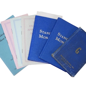 May include: A collection of vintage books with various colored covers, including blue, pink, and light blue. Some books have text that reads "Standard Monitor" and "One Hundred About F". The books are arranged in a fan shape.