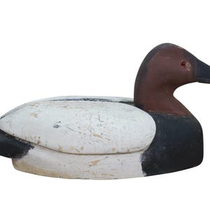 May include: A wooden duck decoy with a white body, black tail and chest, and a brown head and beak. The decoy has a weathered appearance, suggesting it is vintage or antique. This decorative item is likely used for home decor or as a collectible.