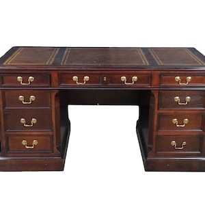 May include: A dark brown wooden pedestal desk featuring a rectangular top with a dark leather inlay and gold-toned border detailing. The desk includes a central drawer flanked by two columns, each containing four drawers with polished brass handles.