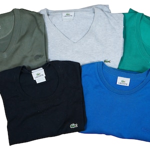 May include: Five folded Lacoste shirts in different colors: green, gray, blue, black, and teal. Each shirt has a small Lacoste logo on the left side of the chest.