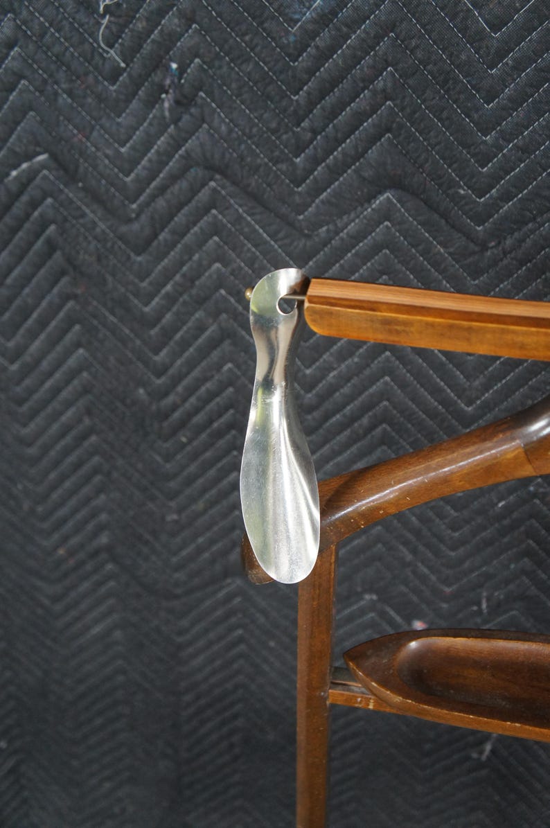 May include: A silver shoe horn hangs from a wooden chair. The shoe horn is a long, curved piece of metal. The chair is made of dark wood and has a curved back and a small tray.