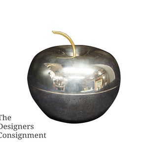May include: A silver apple-shaped trinket box with a gold stem. The box is highly polished and reflects the surrounding environment.