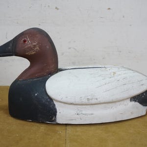May include: A wooden duck decoy, painted in shades of white, black, and brown. The duck has a brown head and a black beak. The body is primarily white with black accents. The decoy is designed to float on water.