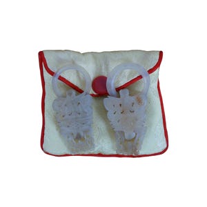 May include: A pair of white jade pendants with intricate carvings, displayed in a white satin pouch with a red trim.