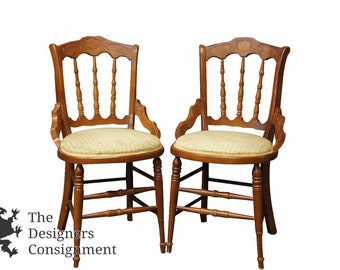 May include: Two wooden chairs with a light brown finish and a beige checkered fabric seat. The chairs have a carved design on the back and a spindle back.