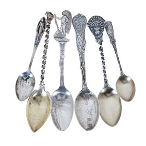 May include: Six silver souvenir spoons with different designs. The spoons feature images of a Native American, a waterfall, a buffalo, a building, and a city skyline. The spoons are all in good condition and have a polished finish.