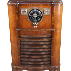 May include: An antique Zenith radio with a wooden cabinet. The radio features a round dial, multiple buttons, and a speaker grill. The cabinet has a curved design and a rich, warm wood grain finish, showcasing a vintage aesthetic.