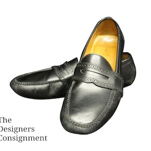 May include: A pair of black leather loafers with a penny strap detail. The loafers have a stitched edge and a brown leather lining.
