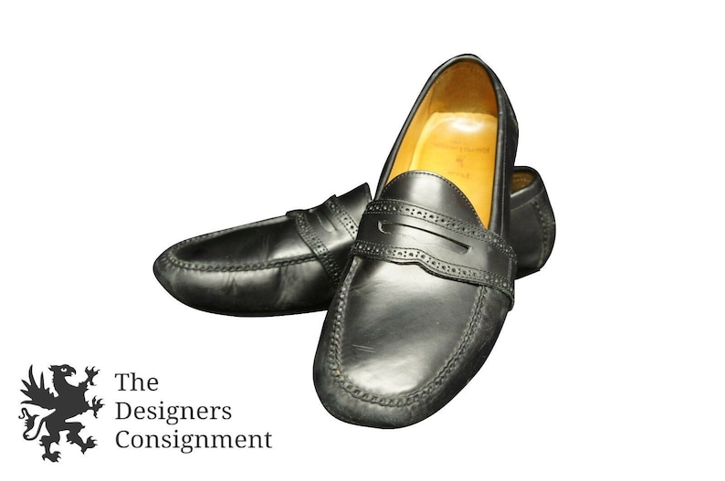 May include: A pair of black leather loafers with a penny strap detail. The loafers have a stitched edge and a brown leather lining.