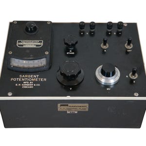 May include: A vintage Sargent Potentiometer, a black rectangular device with various knobs, switches, and a gauge. The device has the text "Sargent Potentiometer" and "E.H. Sargent & Co. Chicago" printed on it. The device is likely used for electrical measurements.