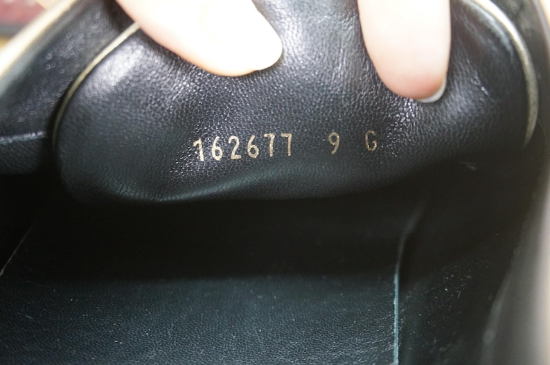 May include: Close-up of the inside of a black shoe. Gold lettering reads "162677 9 G". The shoe's interior is black leather. The image is well-lit, highlighting the details of the shoe's construction.