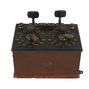 May include: A vintage wooden box with a black metal top and two knobs. The top has a series of numbered dials and switches. The box has a brown wooden base.