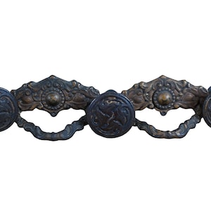 May include: A set of three antique brass drawer pulls with ornate floral designs and round knobs. The pulls are connected by a decorative metal bar.