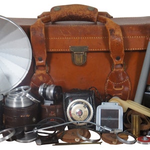 May include: A vintage leather camera bag with a variety of camera equipment, including a flash, lenses, a camera, and a tripod.
