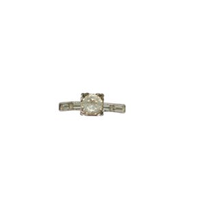 May include: A silver-toned ring featuring a central round-cut clear stone held in a four-prong setting, flanked by two rectangular baguette-cut clear stones on each side of the band, set against a plain white background.