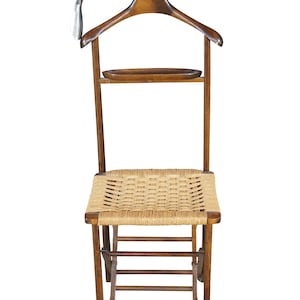 May include: A wooden valet chair with a woven seat and a built-in hanger. The chair has a small shelf and a metal hook. The chair is made of wood and has a natural finish.