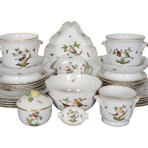 May include: A porcelain dinnerware set featuring white surfaces with hand-painted bird and insect motifs, gold-trimmed edges, and scalloped details. The collection includes lidded bowls, handled cups, saucers, plates, a large serving platter, and a central bowl.