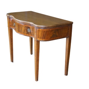 May include: A wooden table with a curved top and a single drawer. The table has a dark wood finish and intricate wood grain patterns.